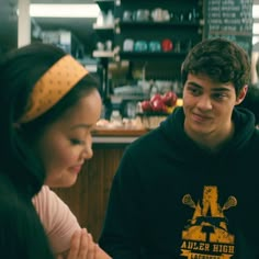 two young people sitting at a table in a restaurant, one is smiling and the other is looking down