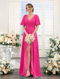 a woman standing in front of flowers wearing a long pink bridesmaid dress with short sleeves