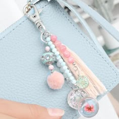 a hand holding a blue purse with charms on it and a keychain attached to it