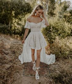 a woman in a white dress is standing on a rug with her hands behind her head