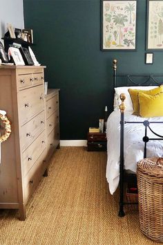 a bedroom with dark green walls and white bedding, wicker baskets on the dresser