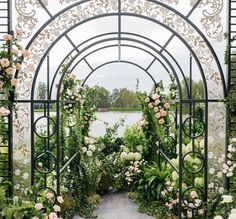 an archway with flowers and greenery on the sides next to a body of water