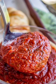 a spoon with some food in it on top of a glass bowl filled with sauce