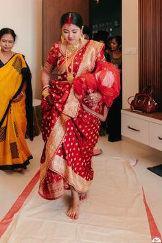 a woman in a red and gold sari walking down the aisle