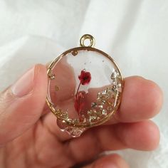 a person holding a glass pendant with a red flower in it's center and gold flecks around the edges