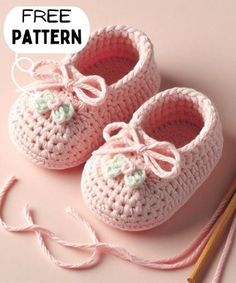 a pair of crocheted baby shoes next to yarn and knitting needles on a pink background