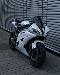 a white and black motorcycle parked in front of a metal wall with shutters on it