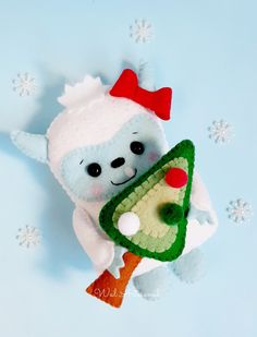 a stuffed animal holding a christmas tree ornament on a blue background with snowflakes