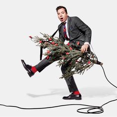 a man in a suit and tie carrying a christmas tree with his feet on the ground