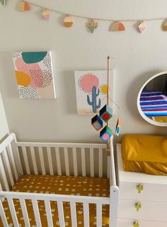 a white crib with a gold sheet on it and some colorful decorations hanging from the wall