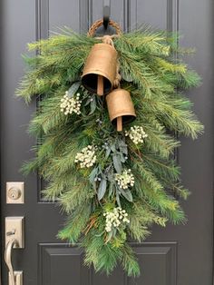 a christmas wreath hanging on the front door with bells and greenery attached to it