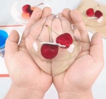 two hands are holding cherries in front of some paint and paper on the table