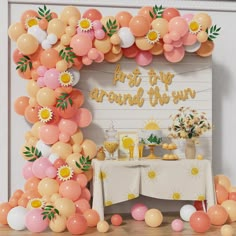 an arch made out of balloons with flowers and sunflowers on the top, in front of a party table