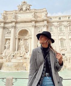 a woman standing in front of a fountain wearing a black and white coat, hat and earphones