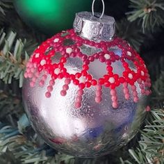 a silver ornament with red beads hanging from a christmas tree