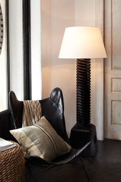 a lamp sitting on top of a table next to a chair with pillows in front of it