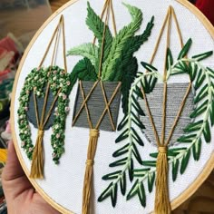 a person holding up a embroidery project with plants in pots on the front and behind it