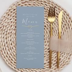 a table setting with silverware and blue menu cards on it, along with gold cutlery