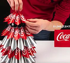 a person is holding a coca - cola christmas tree made out of aluminum cans and wrapped in ribbon