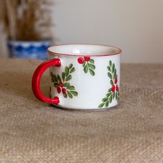 a white and red coffee cup with holly designs on the side sitting on a table