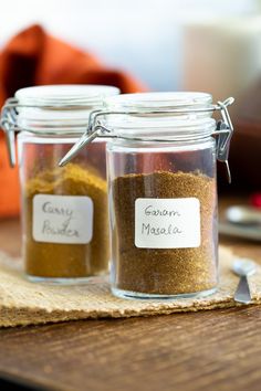 three jars filled with spices sitting on top of a wooden table