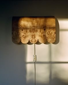 a wooden lamp hanging from the side of a wall next to a window with light coming through it