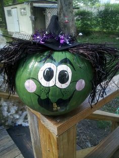 a painted pumpkin with a witch's hat on it sitting on top of a wooden fence