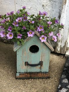 a blue birdhouse with purple flowers in it