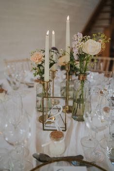 the table is set with wine glasses, candles and flowers in vases on it