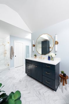 a bathroom with blue cabinets and marble counter tops, gold accents on the mirror over the sink