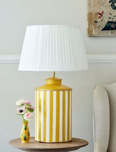 a yellow and white lamp sitting on top of a table next to a vase with flowers