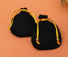 two small black bags with yellow string and beads on the handles are sitting on an orange surface