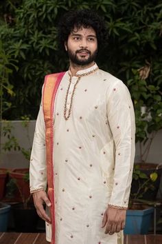 White pattu straight kurta with mandarin collar, full sleeves and floral butti pattern zardozi hand embroidery. Paired with cowl draped dhoti pant with pink kadhua border and a dupatta.
Component: 3
Pattern: Embroidered
Type Of Work: Zardozi and Kadhua Work
Neckline: Mandarin Collar
Sleeve Type: Full Sleeves
Fabric: Pattu
Color: White
Other Details: 
Pink borders
Side slits on kurta
Closure:
Kurta: Front button placket
Dhoti: Elastic waistband
Occasion: Groom, Wedding - Aza Fashions White Chanderi Sherwani For Puja, Navratri Bandhgala With Dori Work And Straight Kurta Style, Navratri Bandhgala With Dori Work, Chanderi Sherwani With Cutdana For Traditional Ceremonies, Cutdana Chanderi Sherwani For Traditional Ceremonies, Sherwani With Cutdana For Traditional Ceremonies, Chanderi Sherwani For Traditional Ceremonies During Navratri, Traditional Chanderi Bandhgala For Ceremonies, Sherwani With Dori Work For Navratri Puja