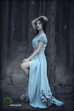 a woman in a blue dress leaning against a tree