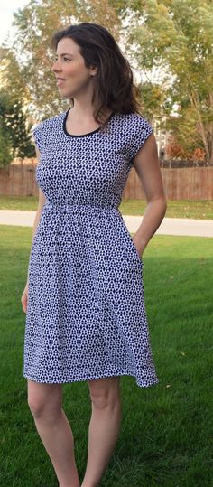 a woman standing in the grass with her hands on her hips, wearing a blue and white dress