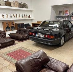 a black car parked in a garage next to two brown leather couches and chairs