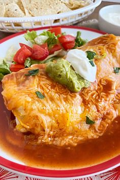 a red and white plate topped with enchilada next to a bowl of salsa