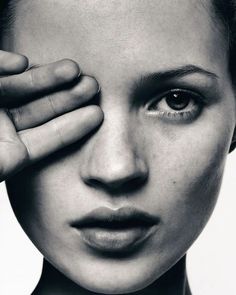 a black and white photo of a woman holding her hand up to her face with one eye open