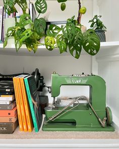 a green sewing machine sitting on top of a table next to books and plants in a room