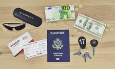 the contents of a passport, keys, sunglasses and money are laid out on a wooden surface