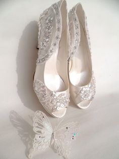 a pair of white wedding shoes next to a butterfly ornament on a white surface