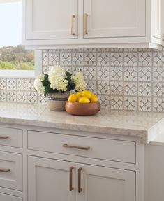 a bowl of lemons and white flowers on a kitchen counter top with cabinets in the background