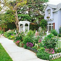 a blue house with white picket fence and flowers in the front yard, on a sunny day