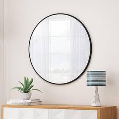 a round mirror hanging on the wall above a dresser with a potted plant in it