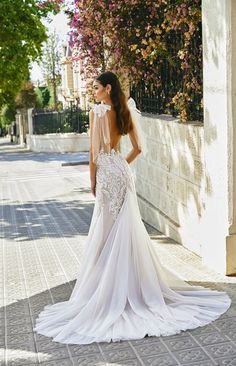 a woman in a wedding dress is standing on the side walk with her back to the camera