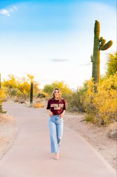 a woman walking down a path in front of a cactus