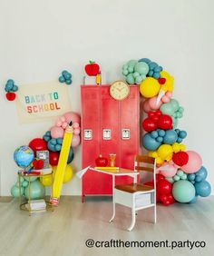 a room filled with balloons and a desk in front of a red school locker next to a white wall