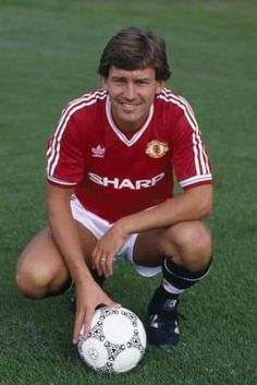 a man kneeling down with a soccer ball in his hand on the grass, smiling