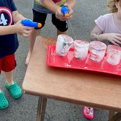 three children are playing with plastic cups and toys on a table in front of them