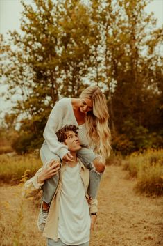 a woman holding a young boy in her arms while he is walking through the woods